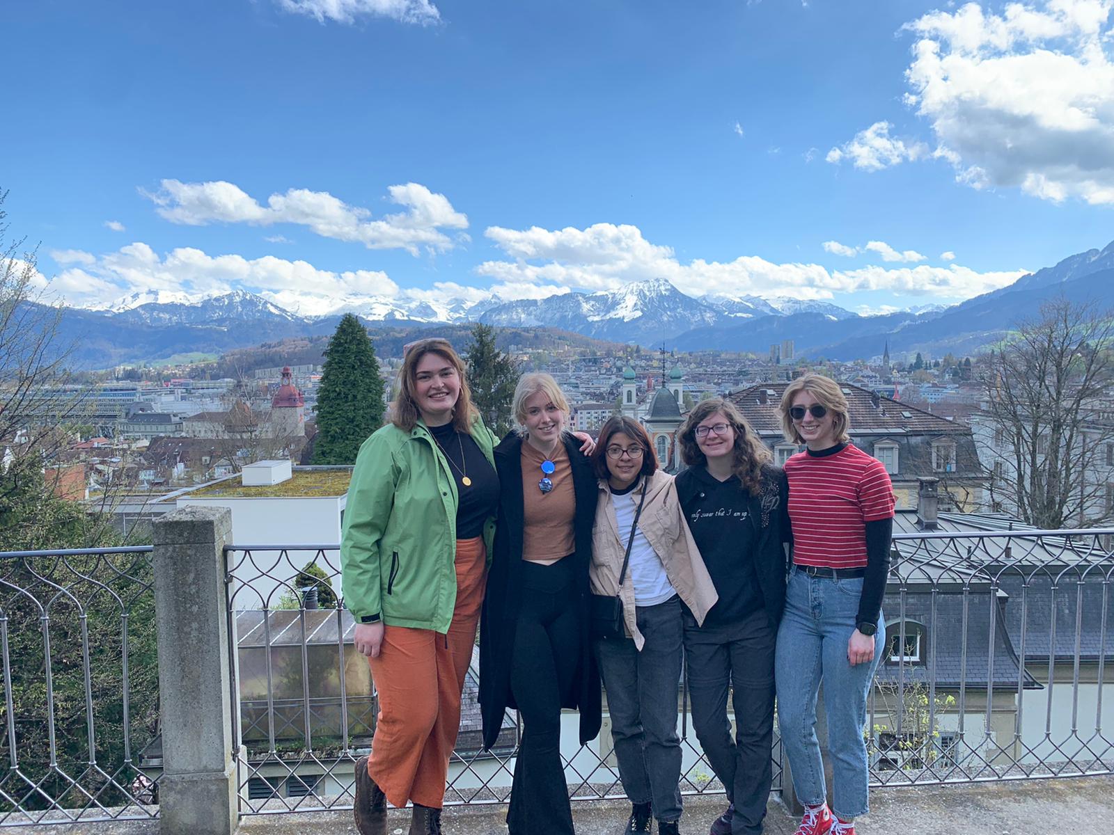 Students posing against a fence with mountains and a small city in the background