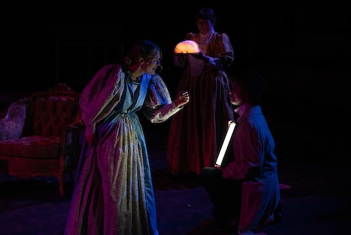 Students in old fashioned gowns under dim colorful lights