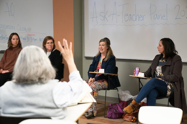 Someone raises their hand to ask a panel of teachers a question