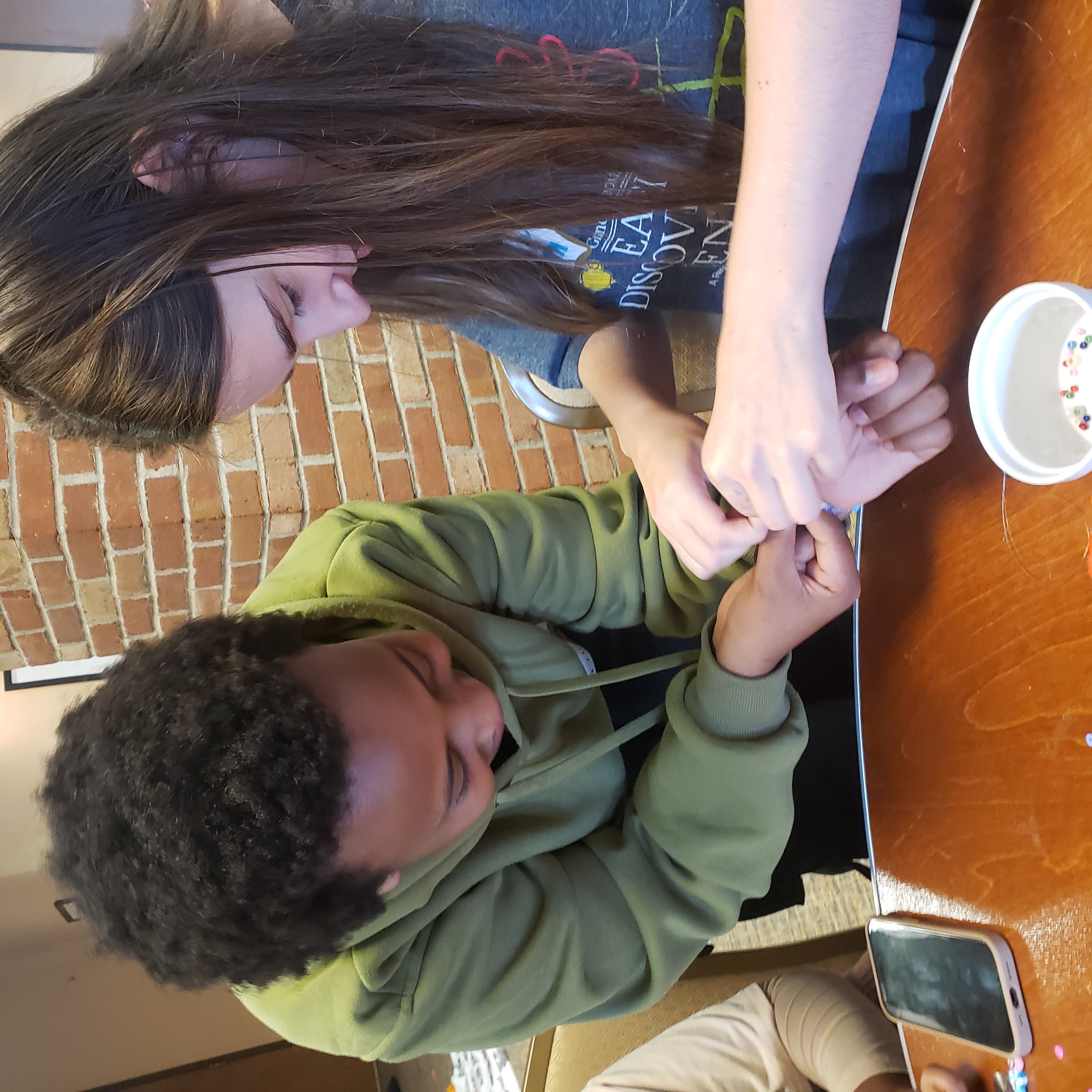 Student and teen put on friendship bracelets